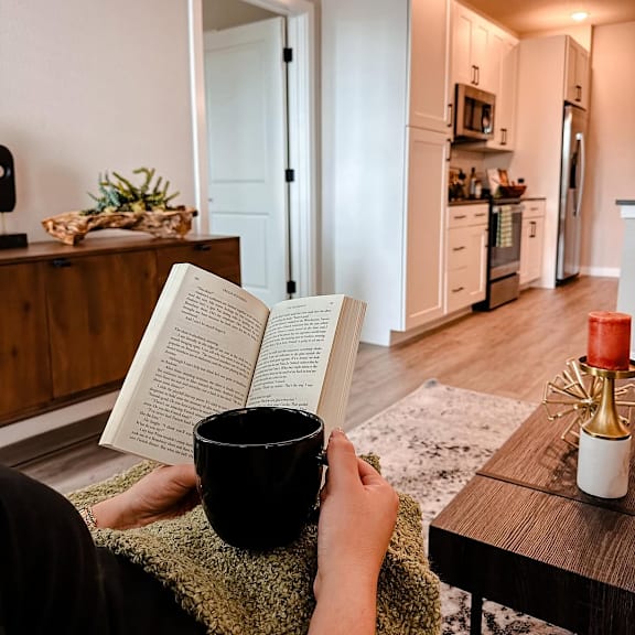 A person is reading a book while holding a black mug.