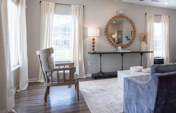 A living room with a grey couch, a chair, a mirror, and a ceiling fan.
