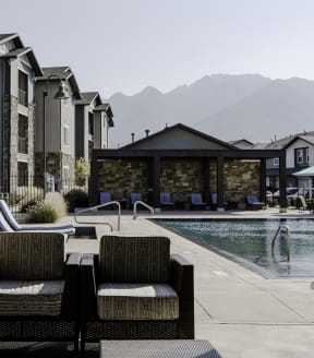 a pool with lounge chairs and umbrellas next to a building with mountains in the background