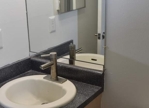 A white toilet with a black seat cover is installed in a bathroom at Sunnymede Apartments in Troy, MI