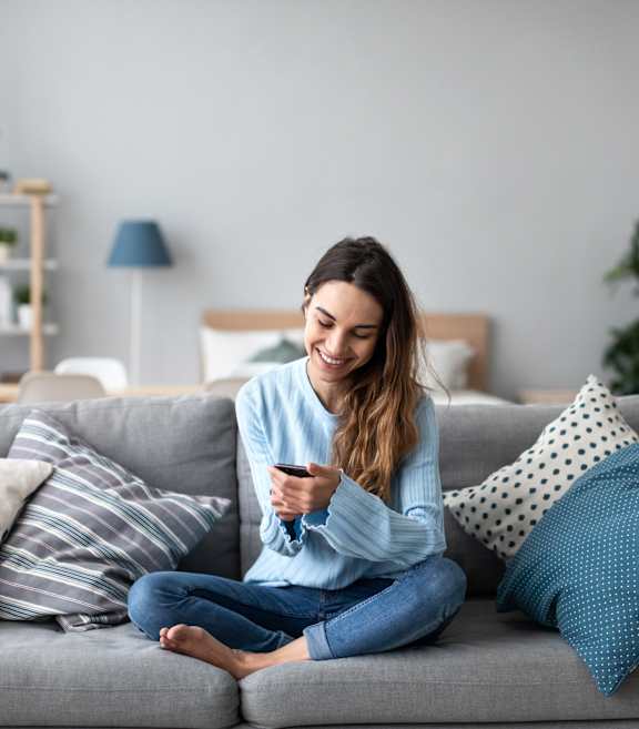 A woman is sitting on a grey couch holding a remote control at Anthem House Apartment, Huntsville, AL, 35806