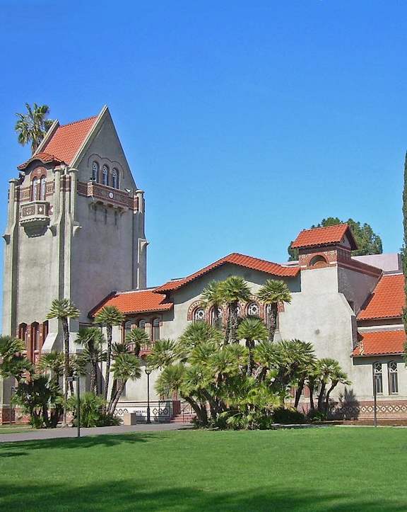 A large building with a tower and a red roof is surrounded by trees.