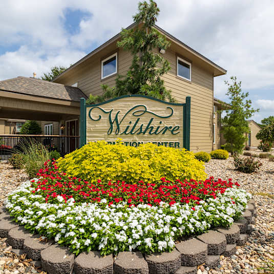 Wilshire Apartments clubhouse exterior featuring a welcoming entrance, large windows, and surrounding landscaping.