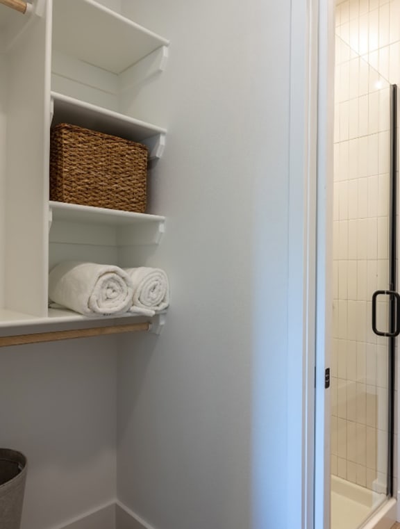 a bathroom with a shower and a toilet and a shelf with towels