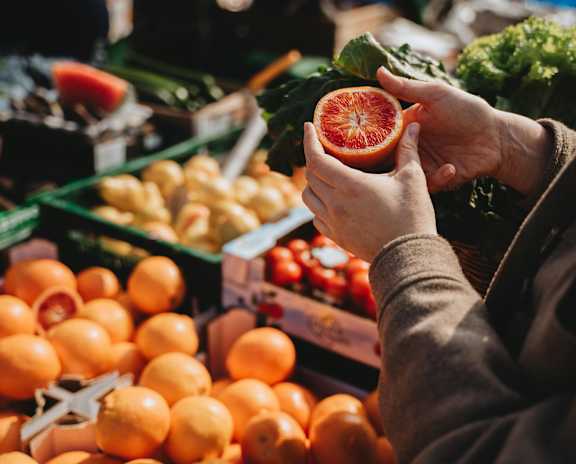 A person holding a grapefruit in front of a display of oranges.