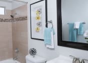 Thumbnail 8 of 23 - Bathroom in one bedroom Fifteen 50 apartments in Las Vegas, 89119 with modern natural tile in bathtub shower and a dark framed mirror above a single sink.