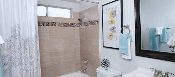 Bathroom in one bedroom Fifteen 50 apartments in Las Vegas, 89119 with modern natural tile in bathtub shower and a dark framed mirror above a single sink.