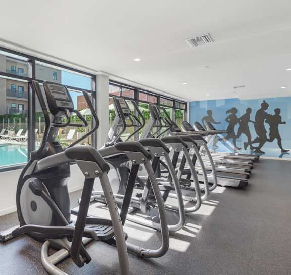 A row of treadmills in a gym with a mural of running people on the wall at Wilshire Valencia Apartment, California