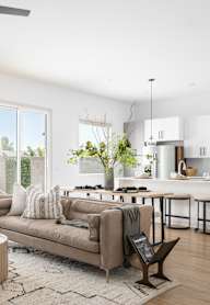 A well-lit, modern living room with a large sofa, a coffee table, and a kitchen area in the background.