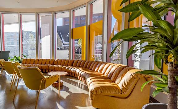 A yellow couch is in the middle of a room with a large window.