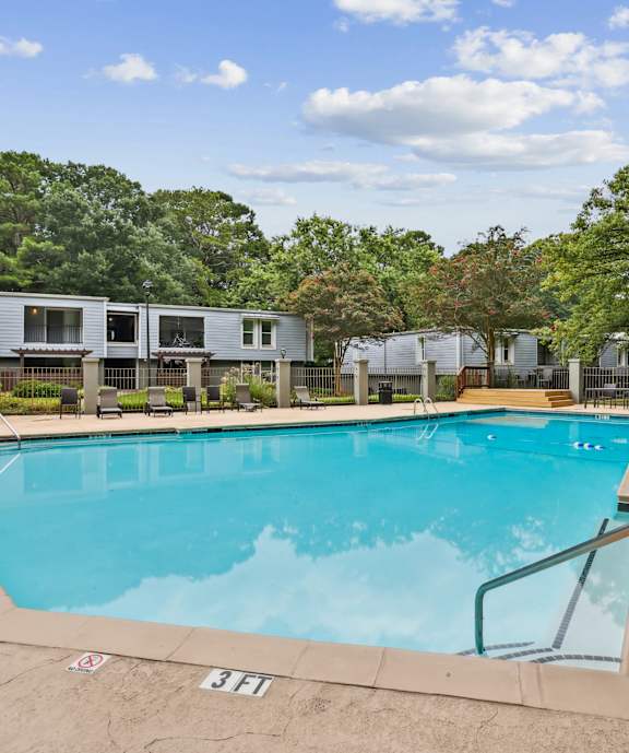 A swimming pool surrounded by trees and a building in the background.