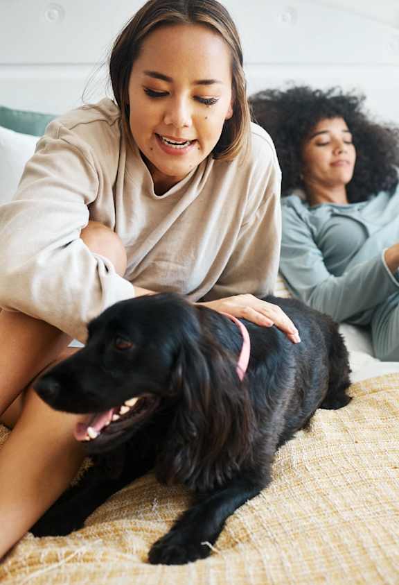 Two women and a dog are relaxing on a bed.
