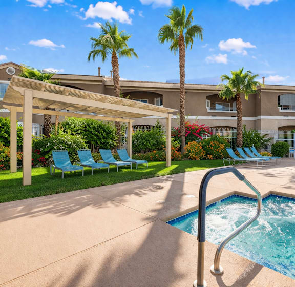 A pool with a slide in front of a house with a patio and lawn chairs.
