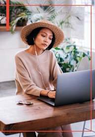 A woman in a straw hat is working on a laptop.