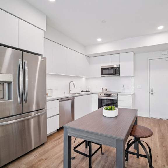 a white kitchen with stainless steel appliances and a wooden table