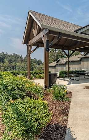 A covered picnic area with a bench and a trash can at Sandyplace Apartment Homes, Sandy, Oregon