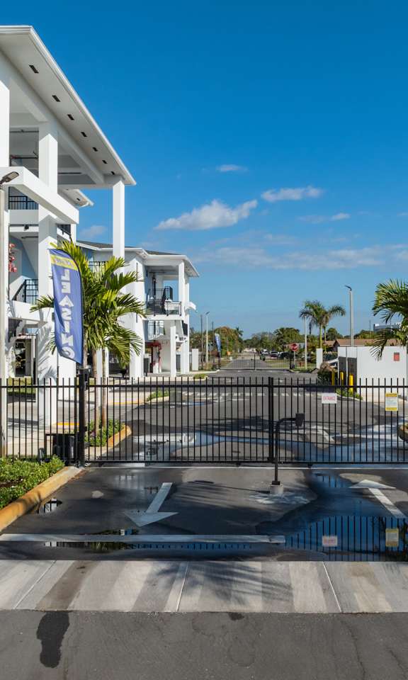 A street view of a residential area with white buildings and a black gate.