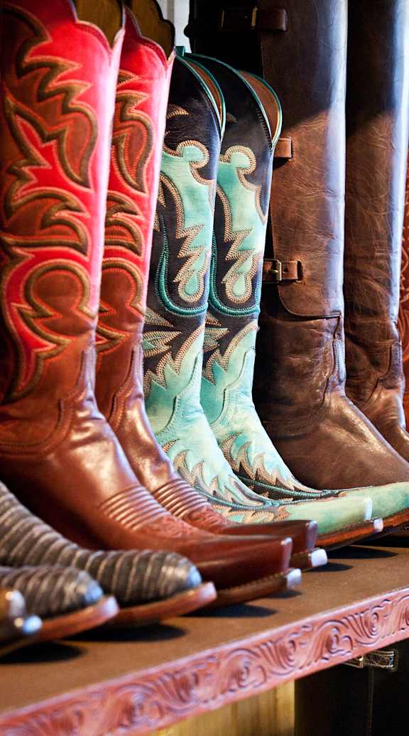 A row of cowboy boots in various colors and designs are lined up on a shelf at Brook Meadow Village, Austin, Texas