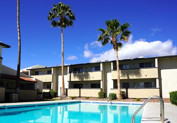 A swimming pool in front of a building with palm trees.