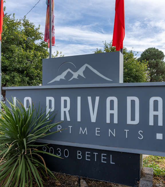 A sign for Privada Artments stands in front of a tree.