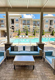 A patio with a table and chairs overlooking a pool and buildings.