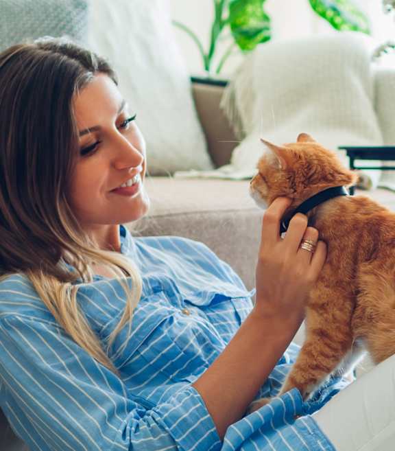 A woman in a blue shirt is sitting on a rug with her orange cat.