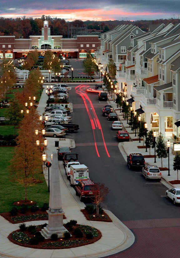 A street view of a shopping area with cars parked on the side of the road.