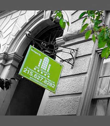 A green sign with white text is hanging from a building.