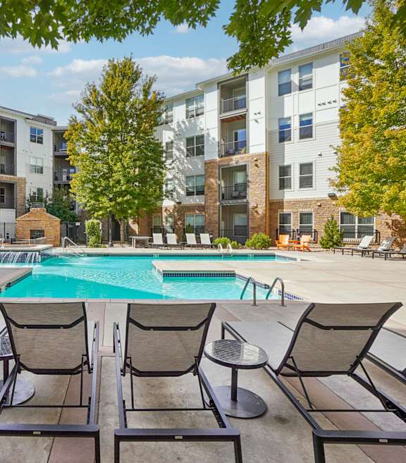 A pool surrounded by chairs and trees in front of apartment buildings.