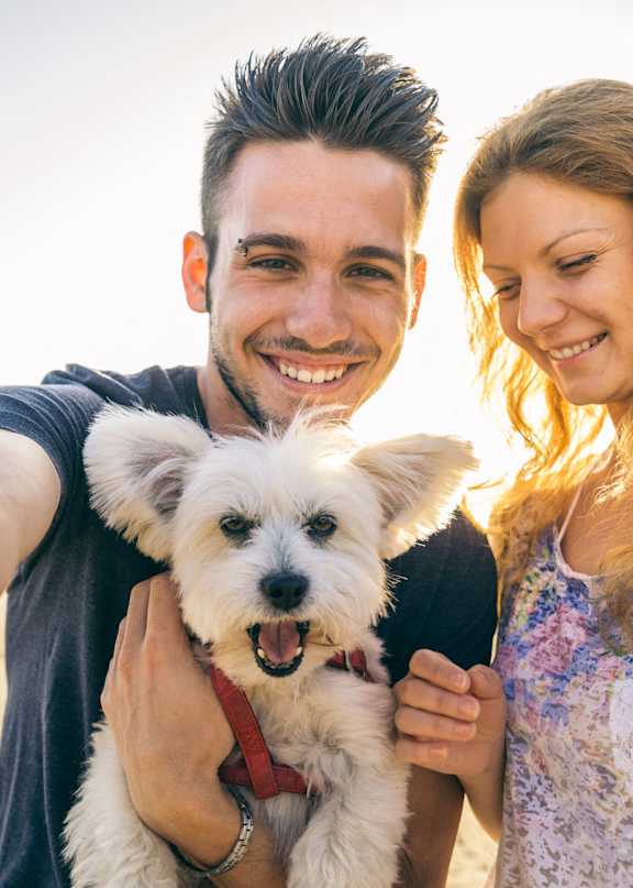 A man and woman are taking a selfie with a small white dog.