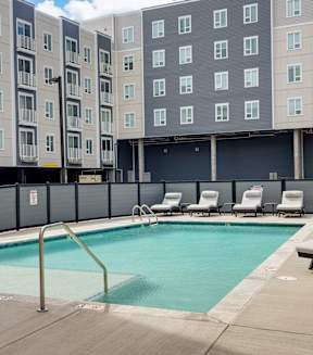 A pool surrounded by chairs and apartment buildings.
