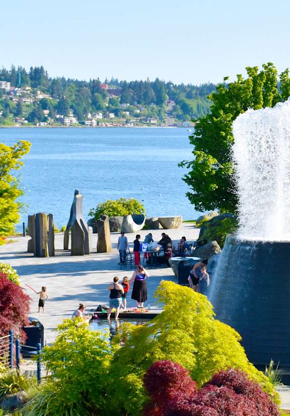 A water fountain in the middle of a park with people around it.