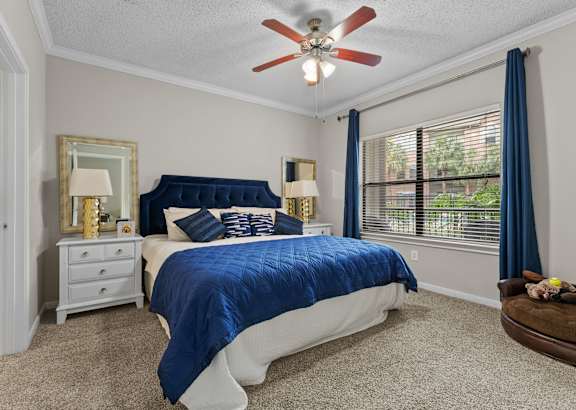 A bedroom with a blue bedspread and a ceiling fan.