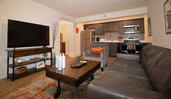 a living room with a couch and a coffee table and a kitchen with a tv
