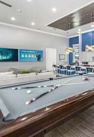 A pool table is in the middle of a room with a kitchen in the background.