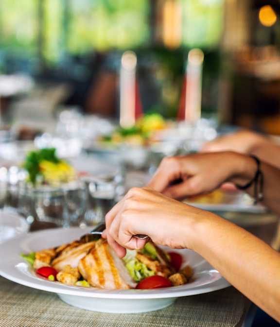 Person is cutting a sandwich on a plate at a table with other plates of food at City-Base Vista, San Antonio, TX, 78223