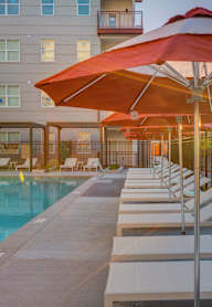 A sunny day at the pool with red umbrellas and lounge chairs.