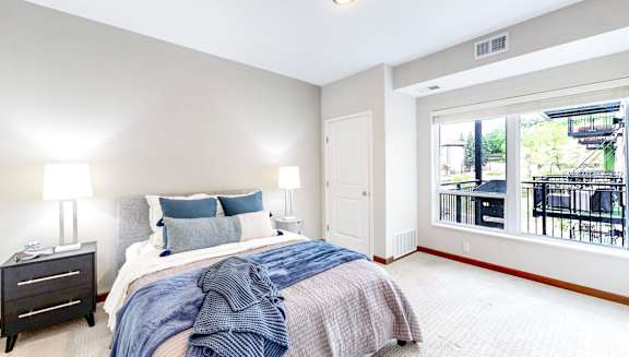 A bedroom with a bed, nightstand, and a window overlooking a balcony.