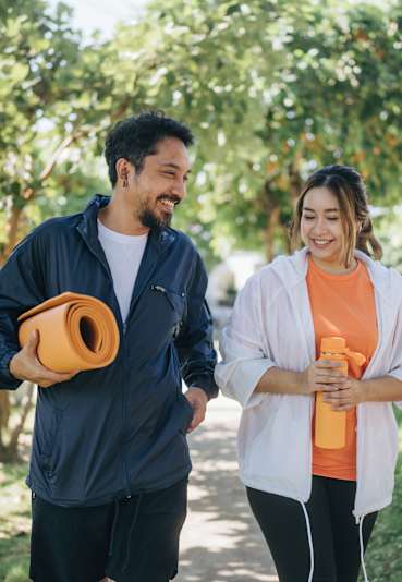 A man and a woman are walking in a park holding yoga mats.