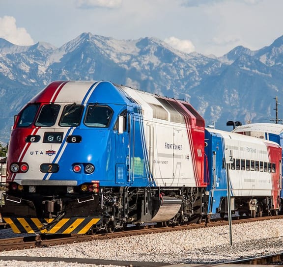 a red white and blue train with mountains in the background