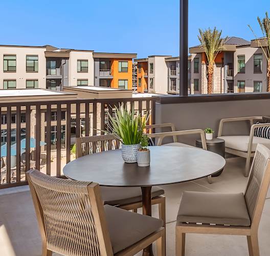 A patio with a table and chairs overlooking a pool and buildings.