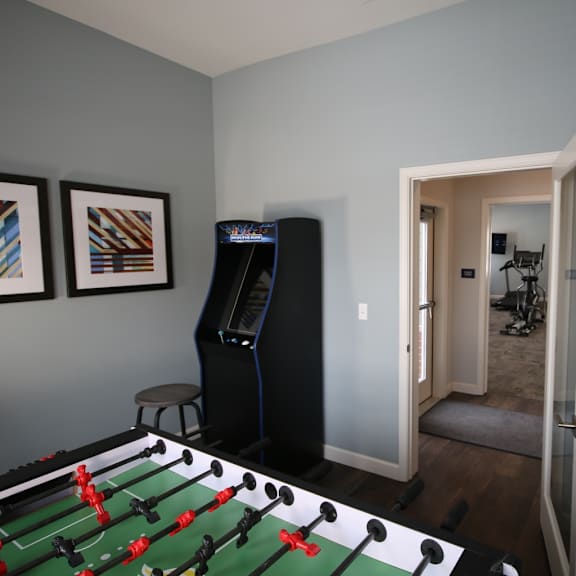 A foosball table is in the middle of a room with a refrigerator and a TV.