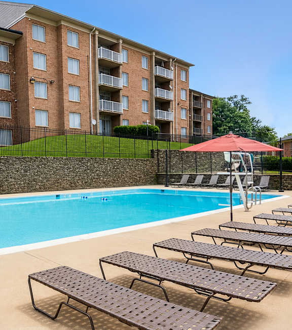 A swimming pool with sun loungers and a red umbrella in front of a brick building.