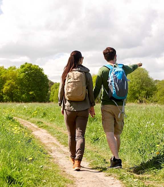 Two people walking on a dirt path through a green field.