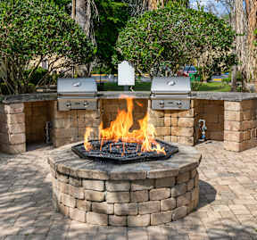 A fire pit in the middle of a brick patio surrounded by brick walls.