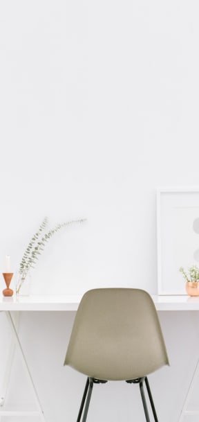 White desk with a plant and picture on it and a chair in front.