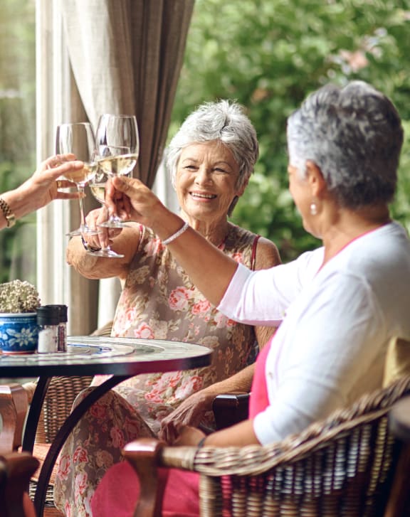 three older women sitting at a patio table drinking wine