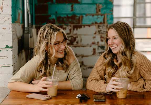 Two women sitting at a table with drinks in front of a brick wall.