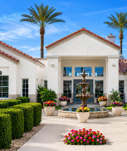 A white house with a red tile roof and a fountain in the front yard.