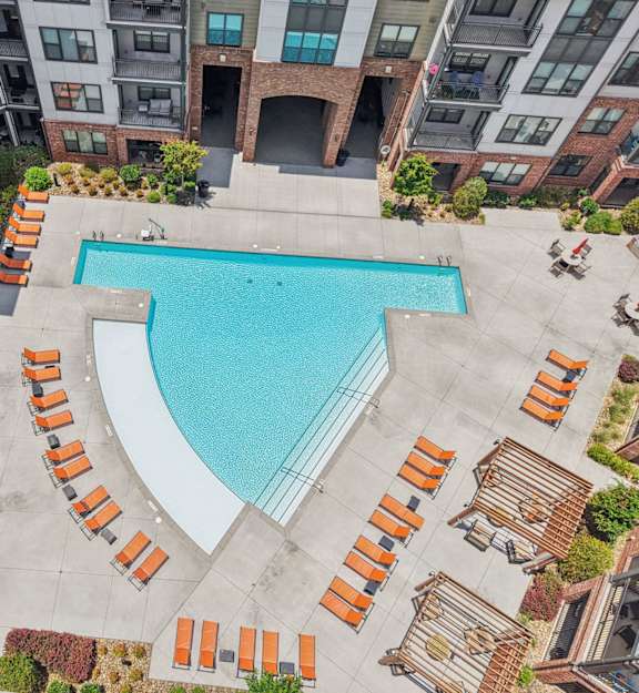 A swimming pool surrounded by orange lounge chairs in a courtyard.